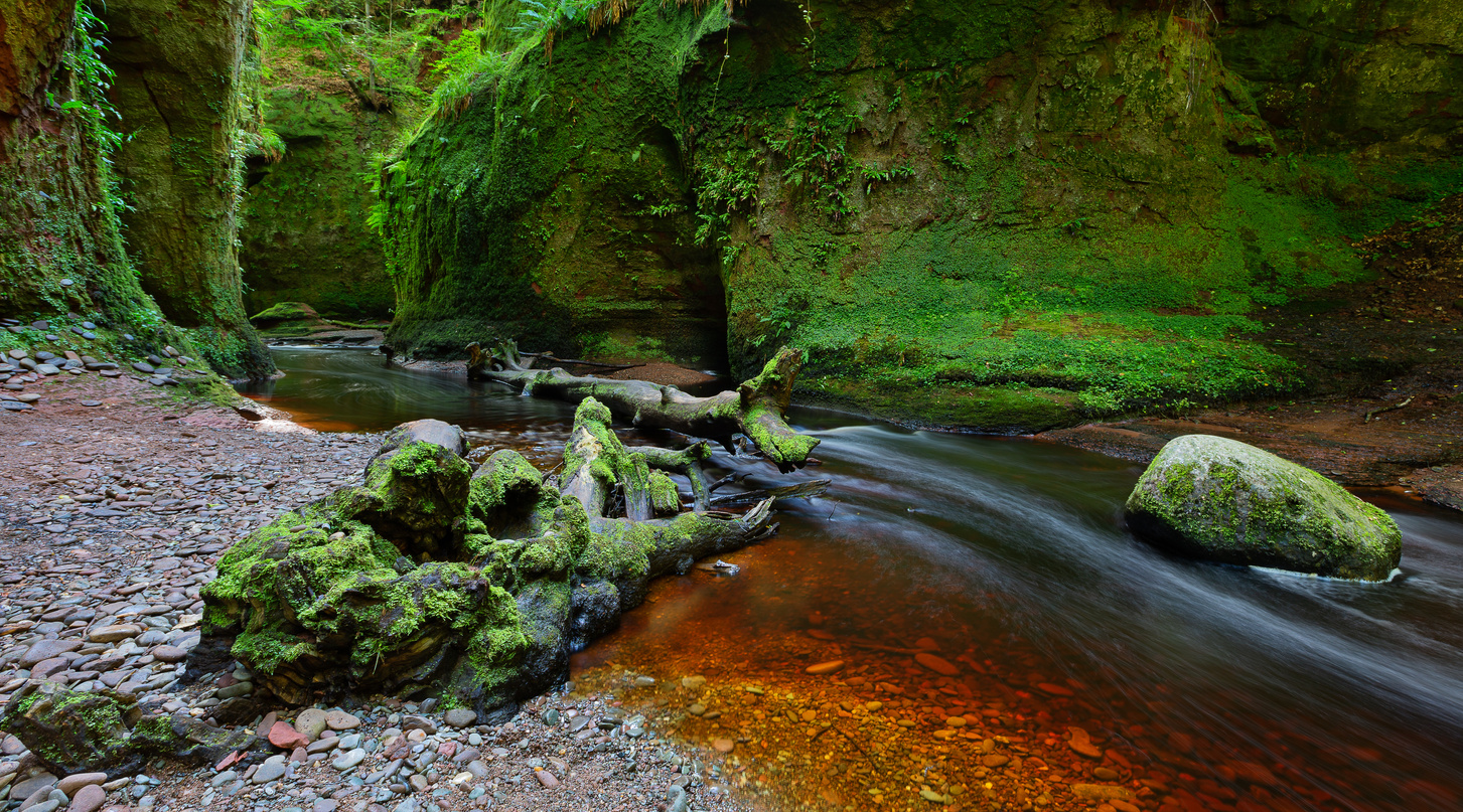 Small river with red water flowing through Finnich Glen landscape photography
